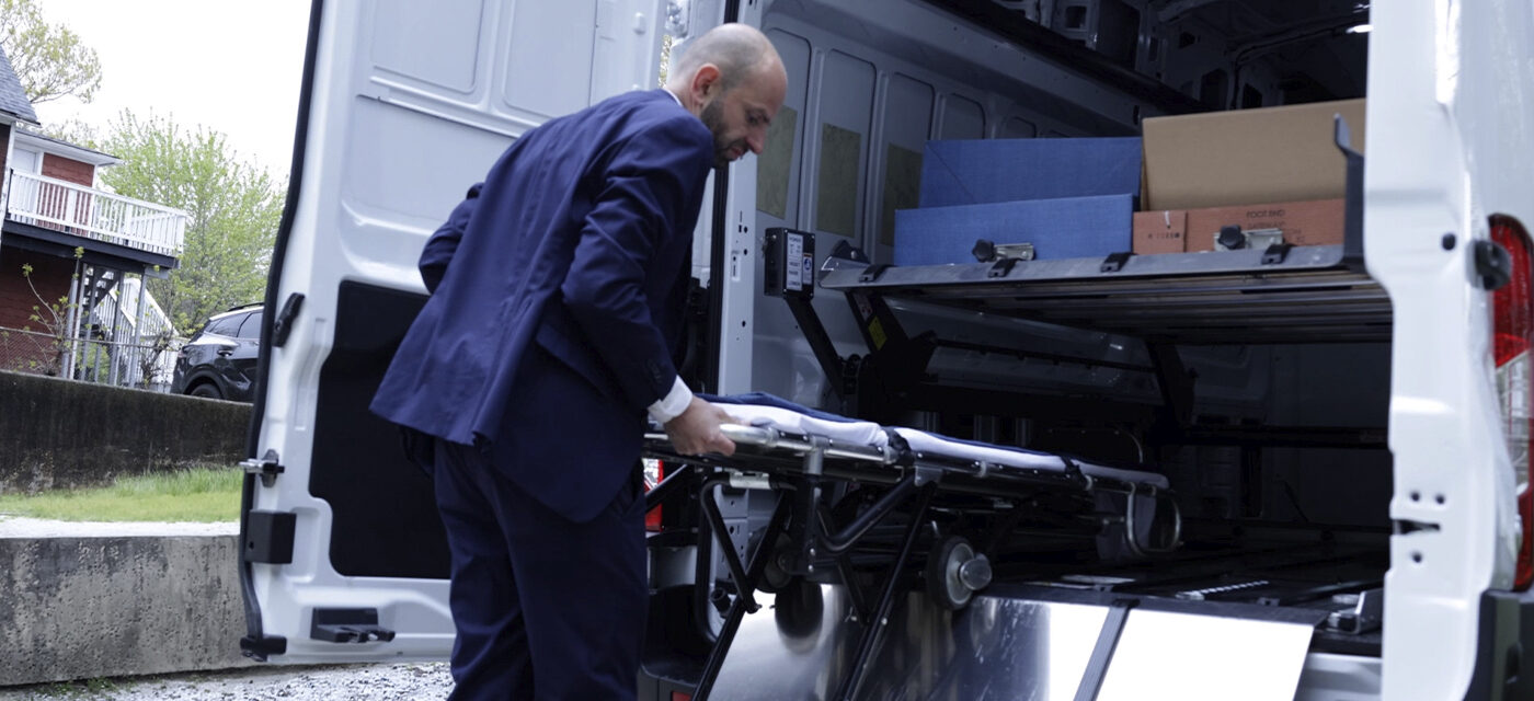 A funeral director loading a cot onto the bottom deck of a DD2000-XLC Double Deck System in a full-sized van