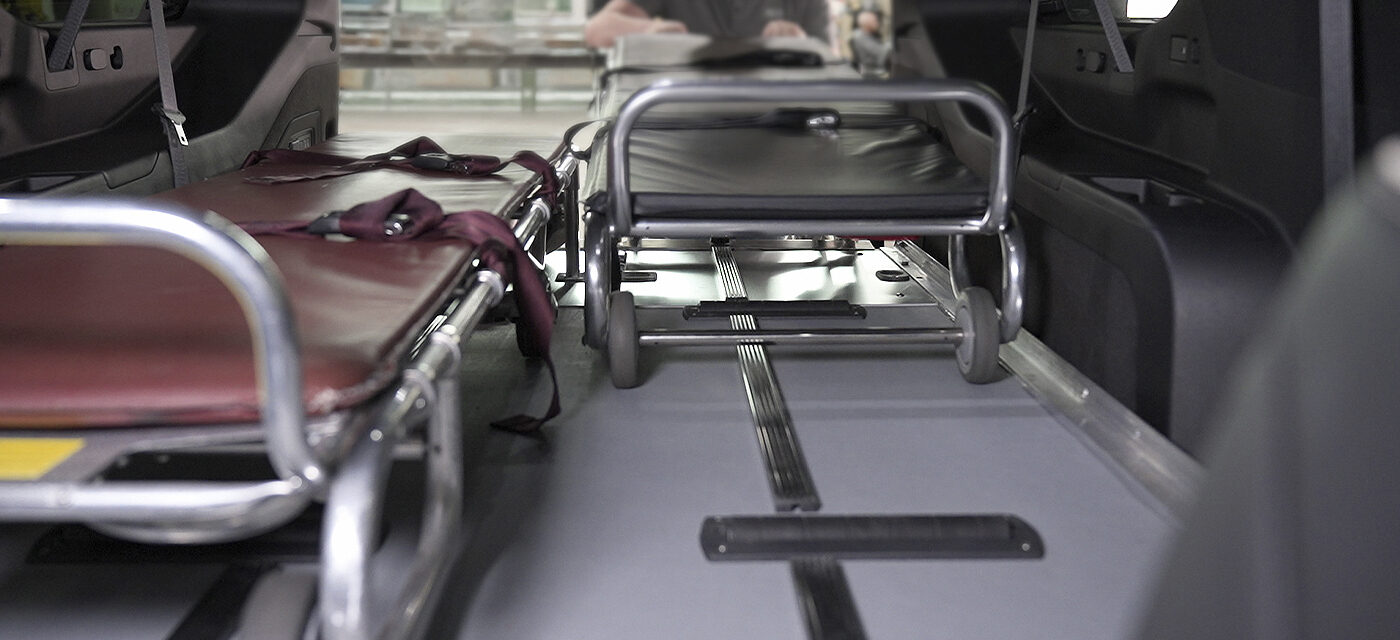 A man loading a cot onto a SS150XL Single Deck System next to an oversized cot in the rear of a SUV