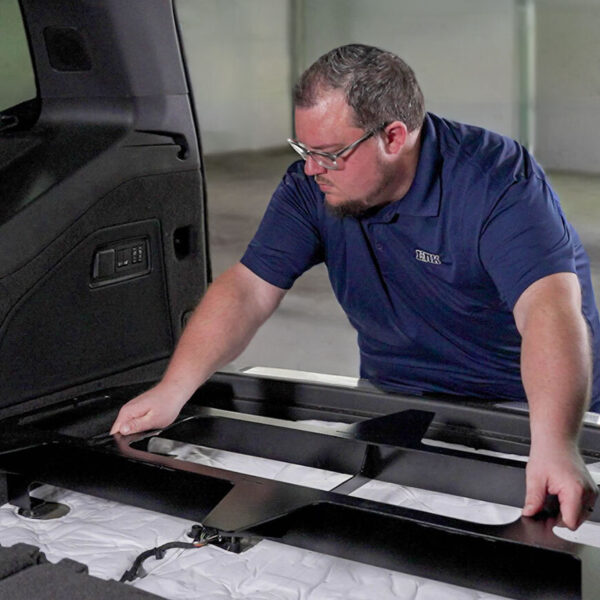 A man installing a SR75 mini deck base in the rear of a Cadillac Escalade utilizing the vehicle's cargo studs